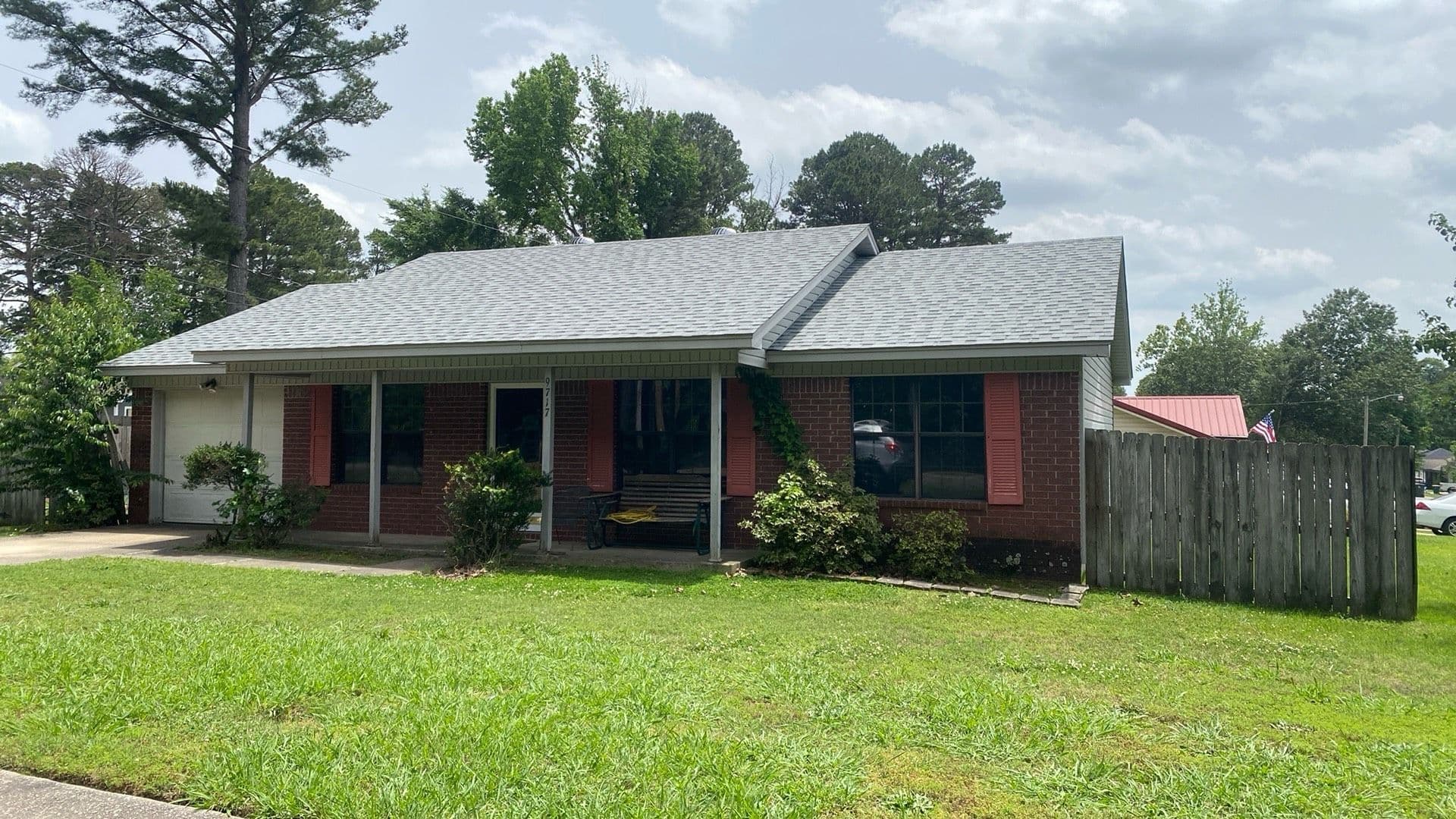 Single-story brick house with a front porch, lush green lawn, and trees nearby.